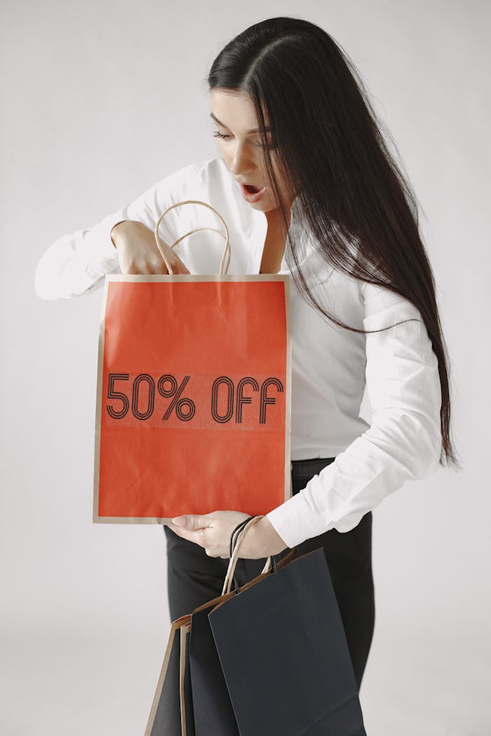 Woman in white shirt excitedly looking into shopping bags with a 50% off sign.